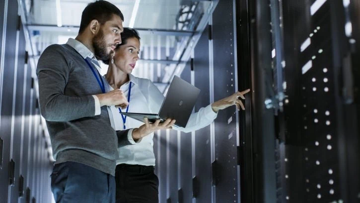 two-persons-in-front-of-a-server Woman and man with laptop stand in front of servers in a data center